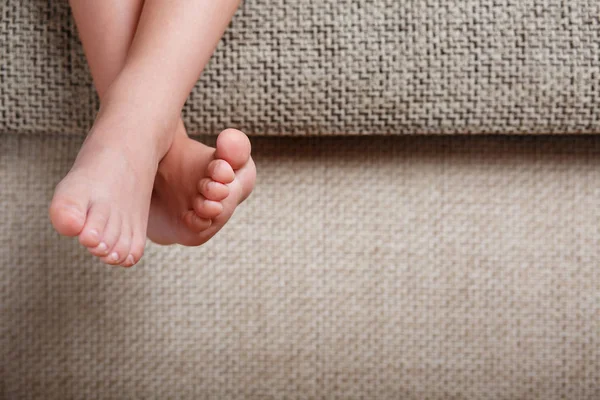 Childrens legs close-up hanging from the sofa in the room. Baby toes while baby is sitting on the armchair