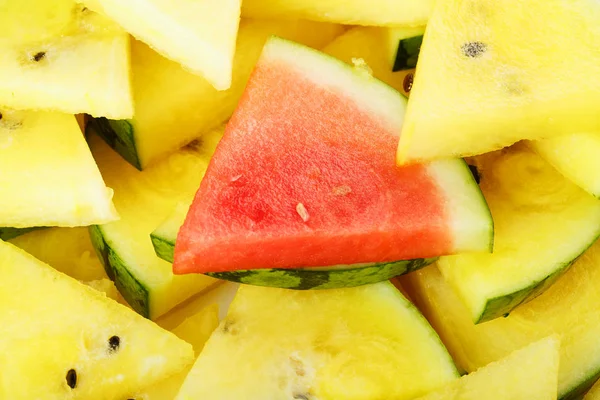 Pieces of red and yellow watermelon in a plate. A slice of red watermelon is one among the yellow pieces. Highlight