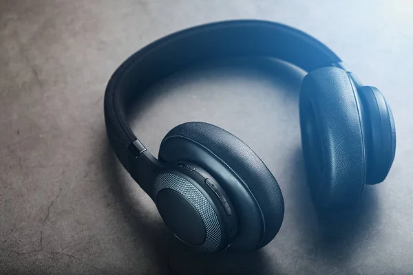 Wireless black headphones on a dark background with blue and orange backlight. On-ear headphones for playing games and listening to music tracks