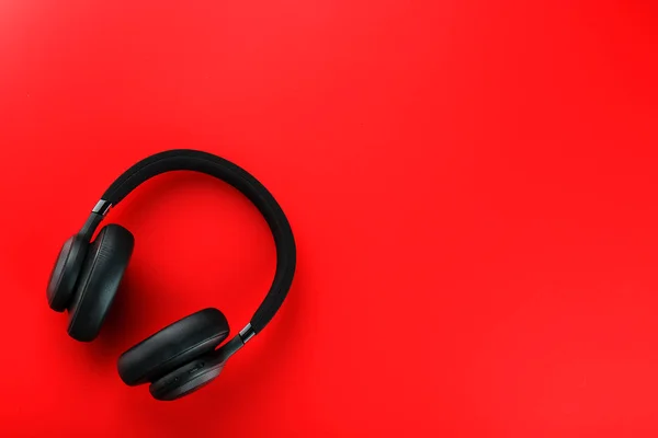 Wireless black headphones on a red background. View from above. In-ear headphones for playing games and listening to music tracks