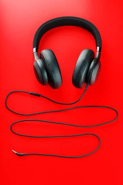 Wireless black headphones on a red background. View from above. In-ear headphones for playing games and listening to music tracks