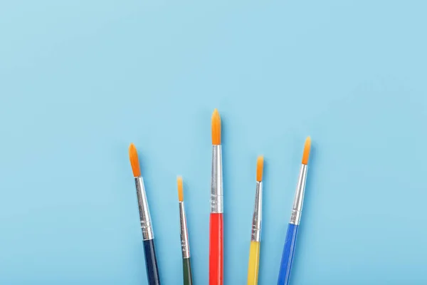 Brushes of different colors for drawing, creativity and art on a blue background. Top view, free space.