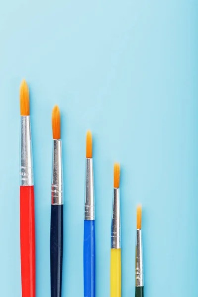 Brushes of different colors for drawing, creativity and art on a blue background. Top view, free space.