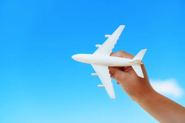 A white toy plane in a child\'s hand against a blue sky. The concept of a dream of travel and flights. Free space.