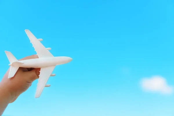 A white airplane in a child\'s hand against a blue sky. The concept of a dream of travel and flights. Free space.