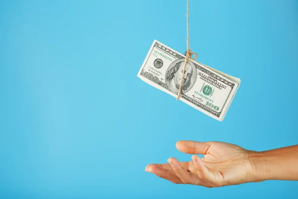 A wad of dollars on a string above a human palm on a blue background. Free space