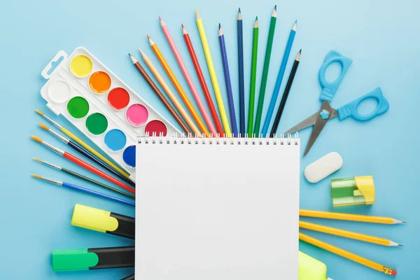 An album for drawing and creativity for school with stationery, a palette of colored paints, markers, brushes and pencils. Free space for text on a blue background. The view from the top