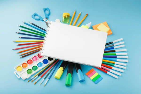 An album for drawing and creativity for school with stationery, a palette of colored paints, markers, brushes and pencils. Free space for text on a blue background. The view from the top