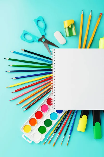 A set of school supplies for learning and creative development on a blue background. Free space on the white album, the view from the top