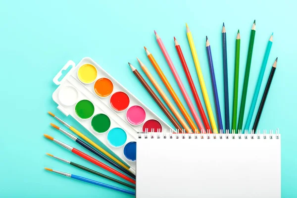 An album of brushes and paints with school supplies on a blue background. Album, a place to copy space. Watercolors, pencils, markers, brushes, and drawing supplies. School is coming soon.Creative approach to children.