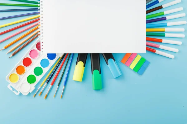 An album of brushes and paints with school supplies on a blue background. Album, a place to copy space. Watercolors, pencils, markers, brushes, and drawing supplies. School is coming soon.Creative approach to children.