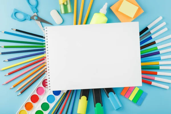 An album of brushes and paints with school supplies on a blue background. Album, a place to copy space. Watercolors, pencils, markers, brushes, and drawing supplies. School is coming soon.Creative approach to children.