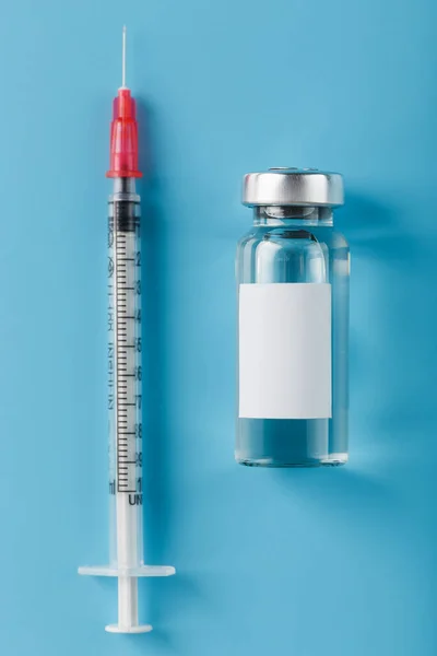 Ampoule with a vaccine and a syringe for viruses and diseases on a blue background. Free space on the ampoule for text. Isolate, vertical frame
