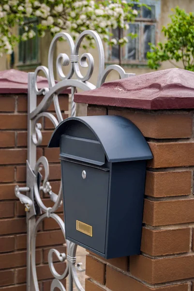 Post metalen doos op een bakstenen hek op de achtergrond van een smeedijzeren — Stockfoto