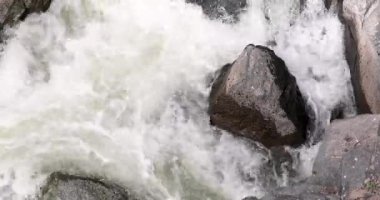 Büyük bir kaya, akan bir nehrin ortasındadır. Su beyaz ve kaya siyah.