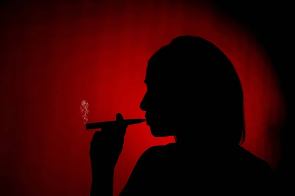 Silhouette of a female smoking an ecig on a red background