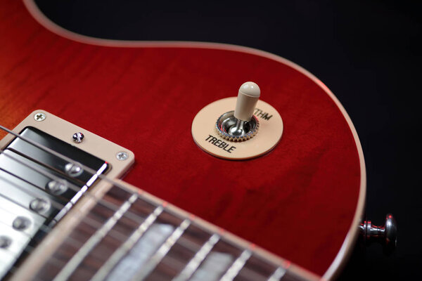 Extreme close up shot of the rhythm and treble switch on a cherry red electric guitar. Mahogany wood body, stainless steel humbucker pickups, aple arch top shape with gloss nitrocellulose lacquer finish.