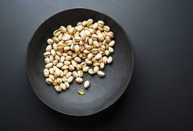 Bowl with pistachios on a black table background clipart