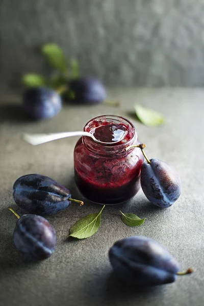 Plum jam or marmalade in a glass jar with plums fruit around