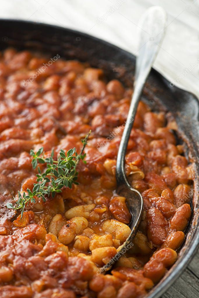 Baked beans stew with tomato sauce and meat with herbs close up