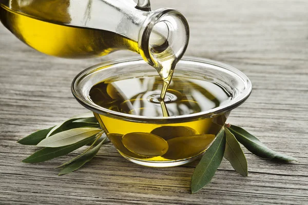 Bottle of Olive oil pouring in a glass bowl with olives