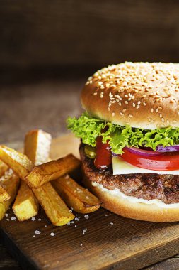 Peynir ve patates kızartması ahşap masa ve koyu arka plan ile lezzetli Hamburger