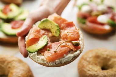 Kadın elinde kremalı simit, avokado ve füme somon balığı tutuyor. Sağlıklı kahvaltı.. 