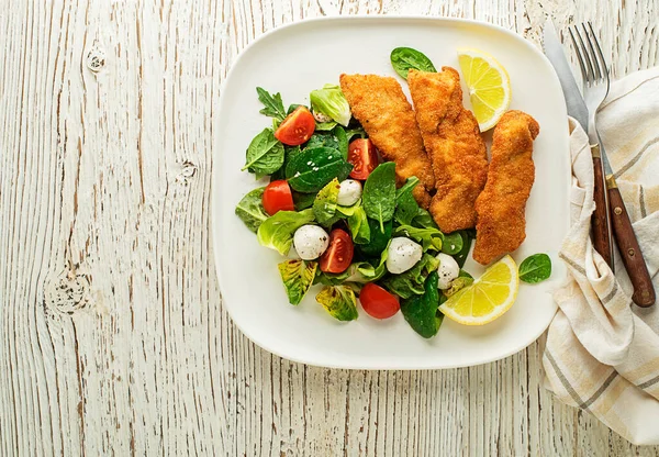 Crispy chicken steaks with green salad and tomato. Fried chicken meal with vegetables