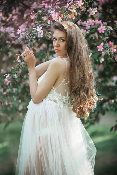 Mujer bonita embarazada está usando vestido de moda blanca posando en el jardín de manzanas de flor rosa, hora de verano — Foto de Stock