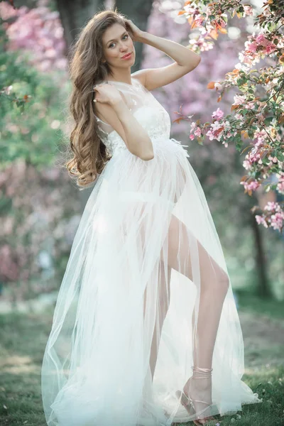 Mujer bonita embarazada está usando vestido de moda blanca posando en el jardín de manzanas de flor rosa, hora de verano — Foto de Stock