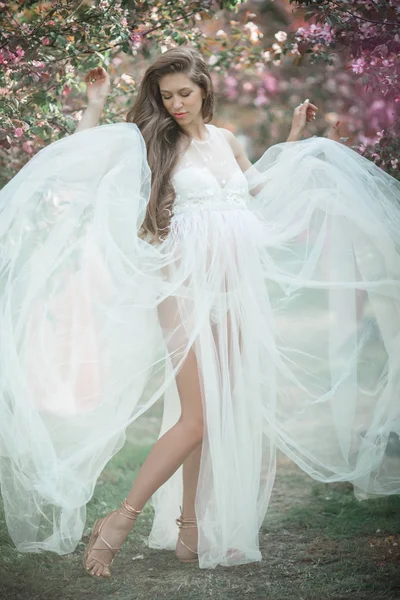 Mujer bonita embarazada está usando vestido de moda blanca posando en el jardín de manzanas de flor rosa, hora de verano —  Fotos de Stock