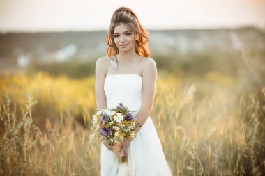 Güzel genç gelin moda alanında günbatımı ışıklar üzerinde çiçekler Buket