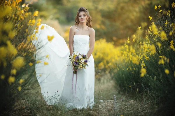 Genç ve güzel gelini sarı alanda kır çiçekleri buketi ile — Stok fotoğraf