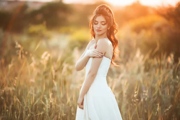 Beautiful young bride with bouquet of wildflowers in field over sunset lights — Stock Photo, Image