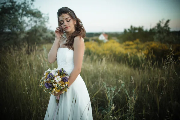 Hermosa novia joven está usando teca con ramo de moda de flores silvestres en el campo amarillo, concepto de boda de la naturaleza — Foto de Stock
