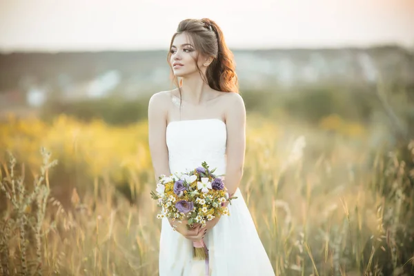 Schöne junge Braut hält Modestrauß von Wildblumen in gelbem Feld, Natur Hochzeitskonzept — Stockfoto