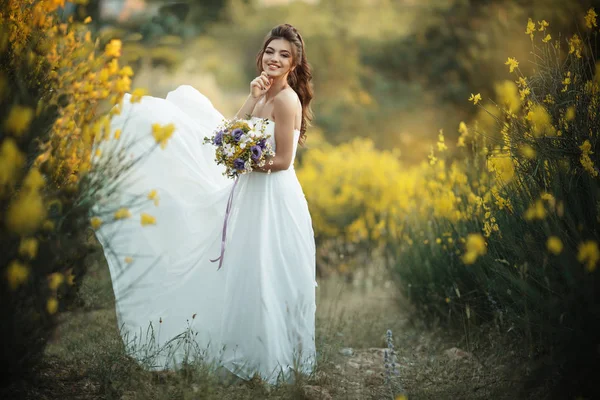 Vackra unga bruden håller mode bukett av blommor i gult fält, natur bröllop koncept — Stockfoto