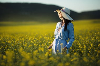 Mutlu genç kadın moda şapka ile kır çiçekleri buketi günbatımı ışıkları sarı alanında giyiyor