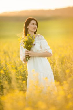 Mutlu genç kadın günbatımı ışıkları sarı alanında kır çiçekleri buketi ile