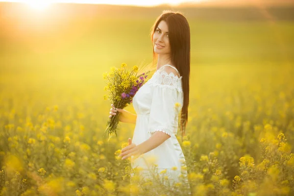 Šťastná mladá žena s kyticí lučních květin v žlutém poli v západu slunce světla — Stock fotografie
