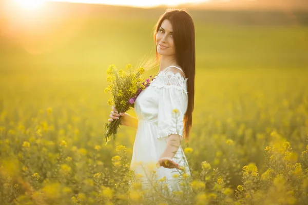 Mutlu genç kadın günbatımı ışıkları sarı alanında kır çiçekleri buketi ile — Stok fotoğraf