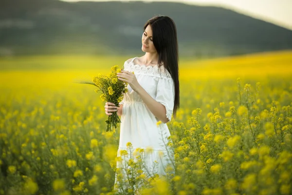 Joyeux jeune femme avec bouquet de fleurs sauvages dans le champ jaune dans les lumières du coucher du soleil, heure d "été — Photo