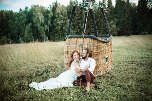 Casal feliz casamento estão sentados perto de cesta de airballoon no campo ensolarado . — Fotografia de Stock