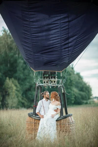 Feliz casamento lindo casal noiva e noivo estão sentados dentro cesta airballoon no campo ensolarado . — Fotografia de Stock