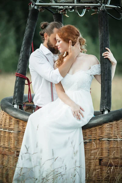 Feliz casamento lindo casal noiva e noivo estão sentados dentro cesta airballoon no campo ensolarado . — Fotografia de Stock