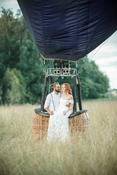 Heureux couple de mariage mariée et marié sont assis à l'intérieur du panier aéroballon dans le champ ensoleillé . — Photo