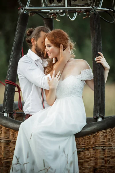 Heureux couple de mariage mariée et marié sont assis à l'intérieur du panier aéroballon dans le champ ensoleillé . — Photo