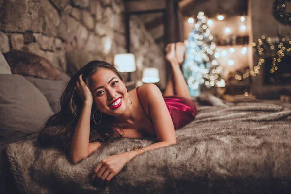 Όμορφη ασιατική γυναίκα κάθεται στο σπίτι κοντά στο χριστουγεννιάτικο δέντρο στο άνετο εσωτερικό. Εσωτερικό με χριστουγεννιάτικα στολίδια. — Φωτογραφία Αρχείου