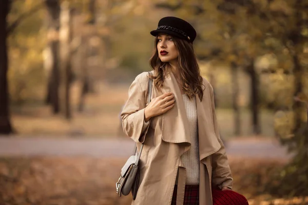 Pretty stylish woman with fashion makeup in autumn park is wearing hat and coat — Stock Photo, Image