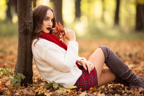 Mujer bonita está usando ropa de moda sentado en el parque de otoño —  Fotos de Stock